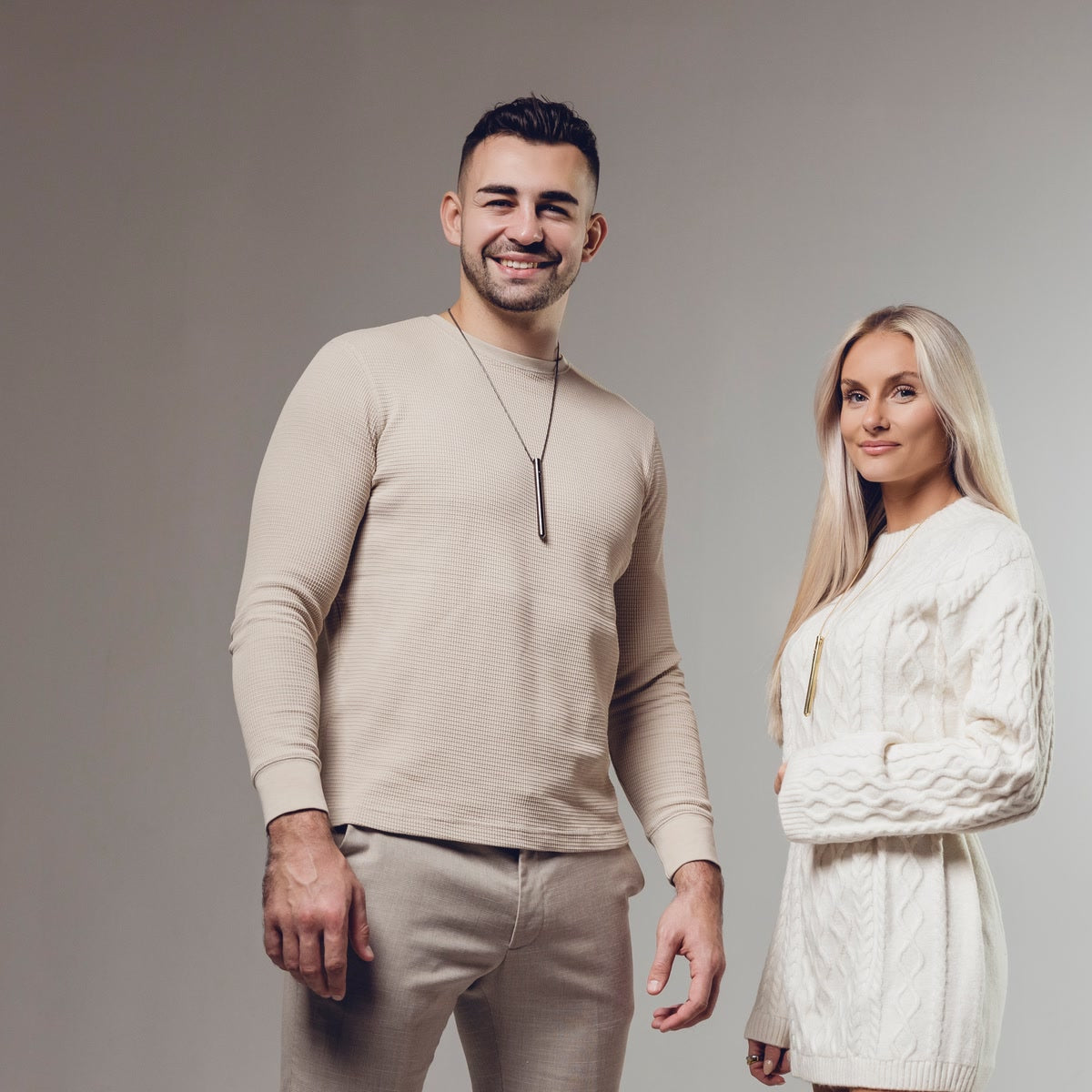 Ein Mann und eine Frau tragen die EASE Kette über dem Pullover